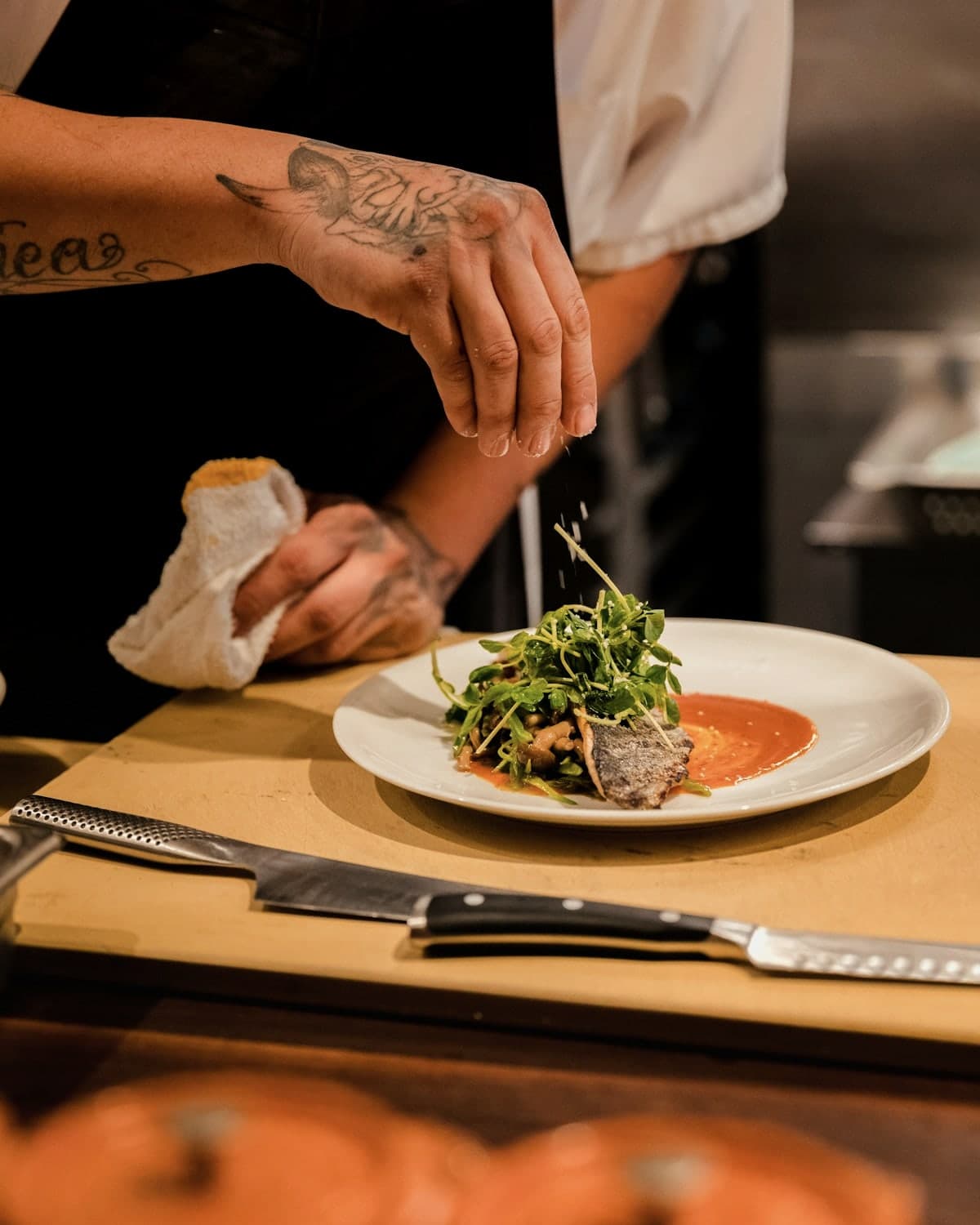 A kitchen pass: hands finishing a plate for service