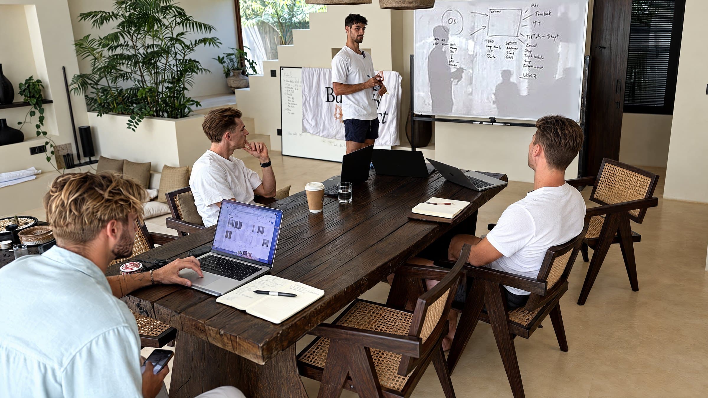 Alex Kaymakanov at the whiteboard walking The Butterfly Effect team through the operating system design, the team at the table with laptops open